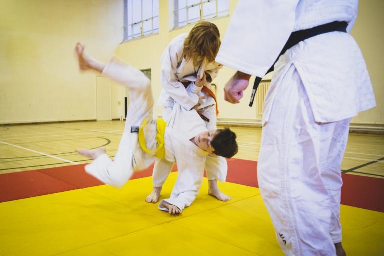 Image shows instructor supervising two children performing a judo throw.