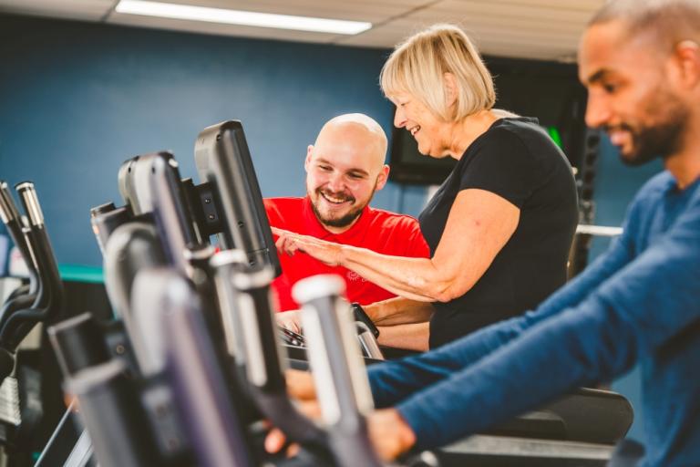 Lady on cross trainer being instructed by gym instructor.