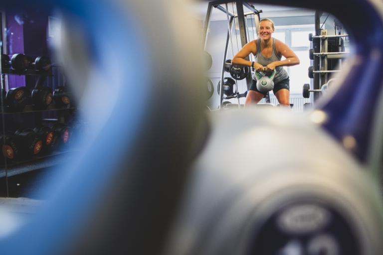 Image shows reflection of woman lifting a kettle bell weight.
