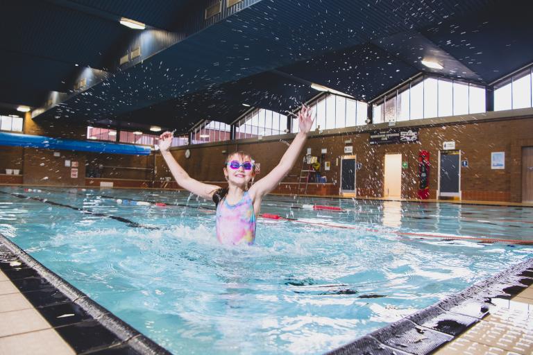 Image shows girl splashing and having fun in a swimming pool.