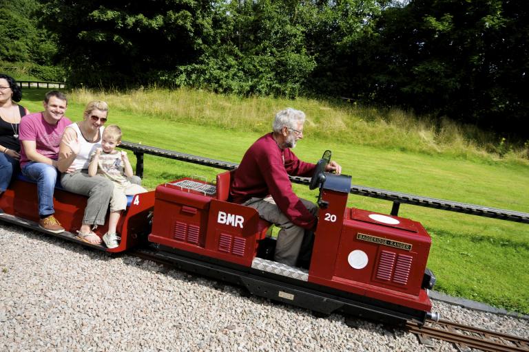 Image shows miniature train in motion with customers sat riding on it.