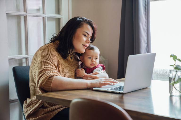 A woman uses her computer while holding a young child