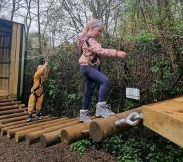 children balancing on a wobbly log bridge