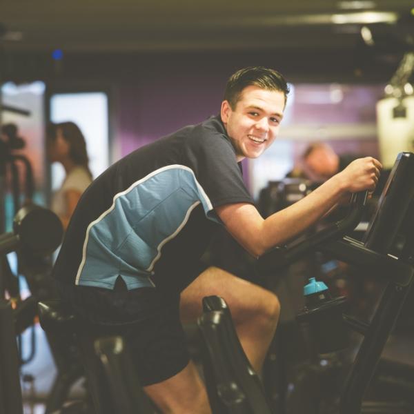Image shows teenager sat on exercise bike in gym 